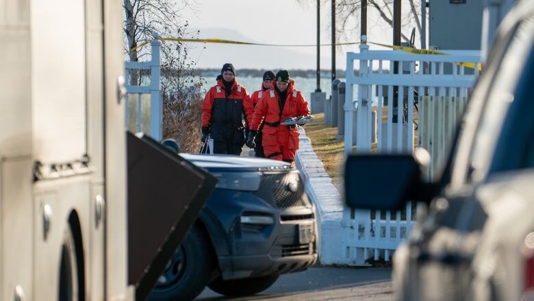 People wearing orange suits walk toward a parking lot. Behind them is yellow police tape.