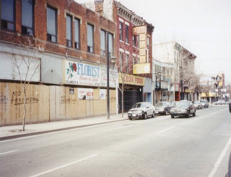 cars drive past boarded up shop windows