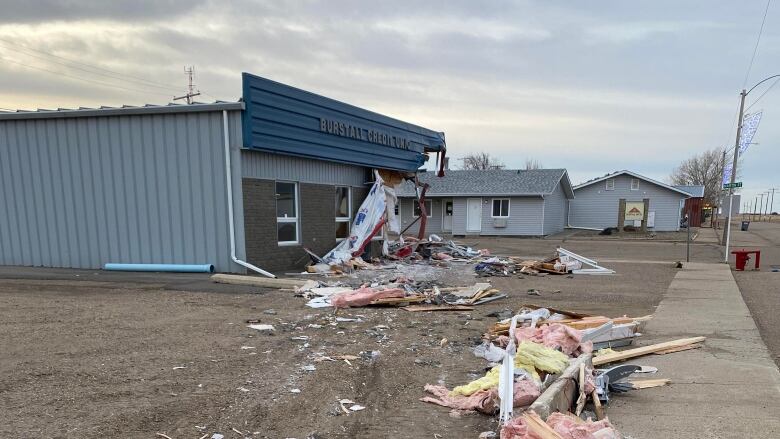 A building sits with its corner torn out, debris scattered in the foreground.