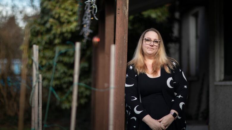 A woman leans against a post.