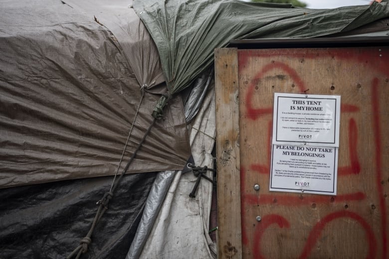 A sign affixed on a makeshift tent reads 'This Tent is My Home, Please Do Not Take My Belongings' along with smaller text.