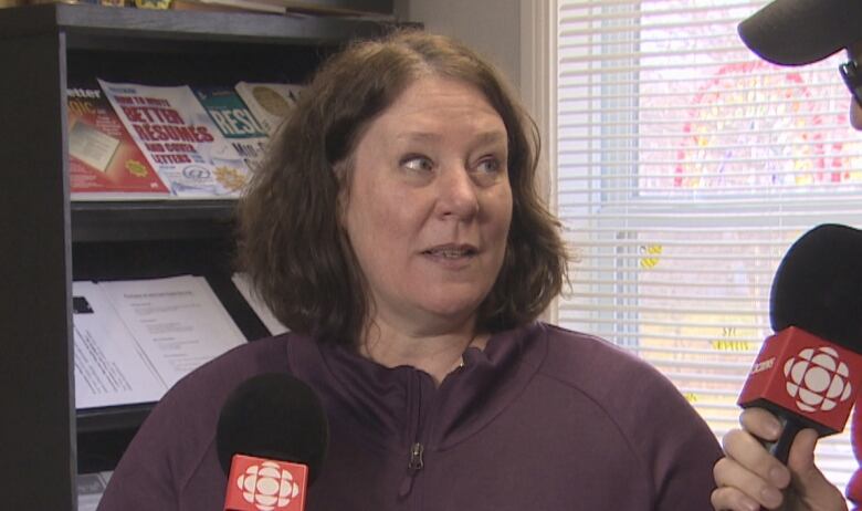 A woman with brown hair and a purple shirt speak into a microphone