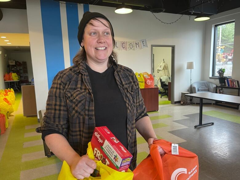 A woman stands holding bags of groceries. 