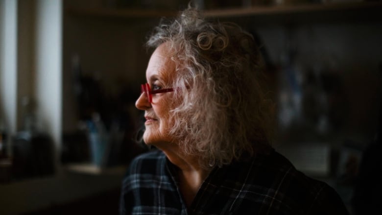 Susanna Blunt, who has curly grey hair in a bob and red-framed glasses, is shown in profile as she looks out a window.