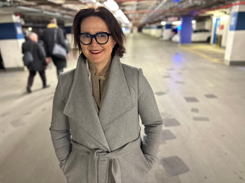 A woman in a jacket stands in an underground parking garage.