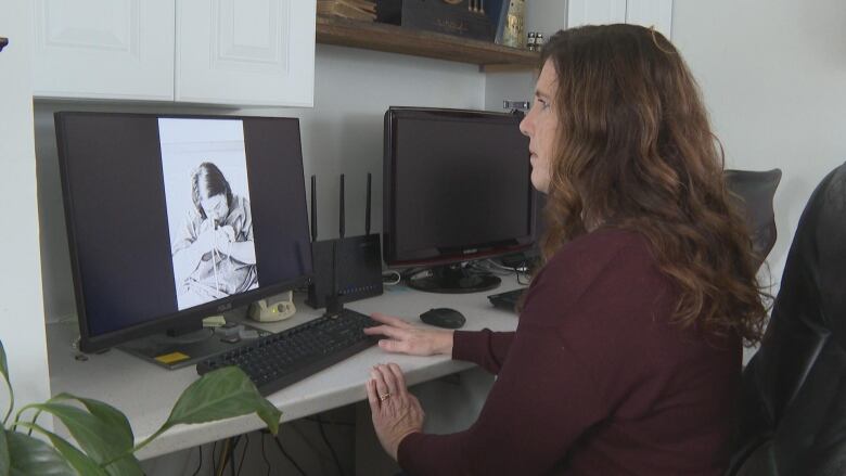 A woman looks at a computer screen where a mom is holding a baby. 