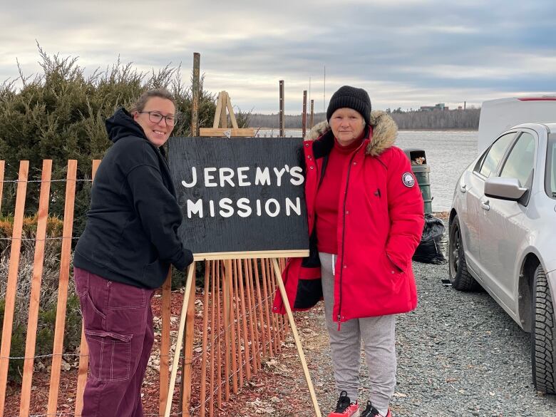 two women standing outside alongside a sign that reads Jeremy's Mission