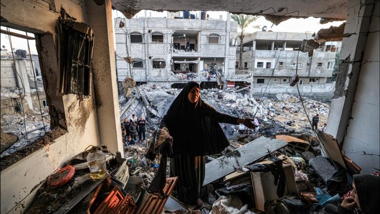 People gesture while standing amid the rubble of a destroyed building.