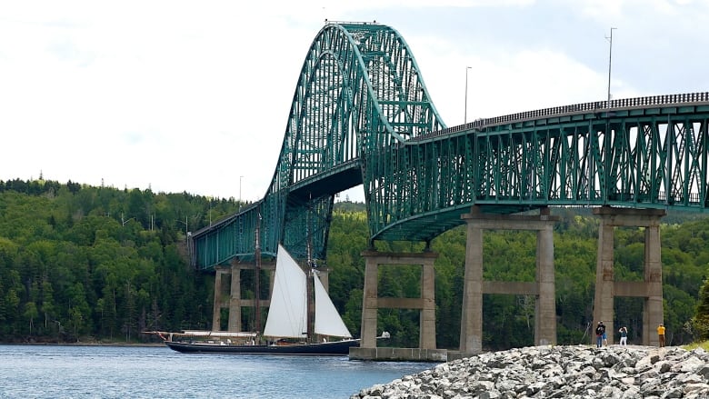 The schooner Bluenose II sails under the Seal Island Bridge while on-lookers take photographs.