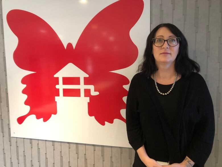 A woman stands in front of a butterfly-like logo