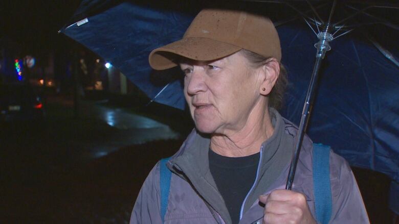 An older white woman holds an umbrella and speaks to a camera.