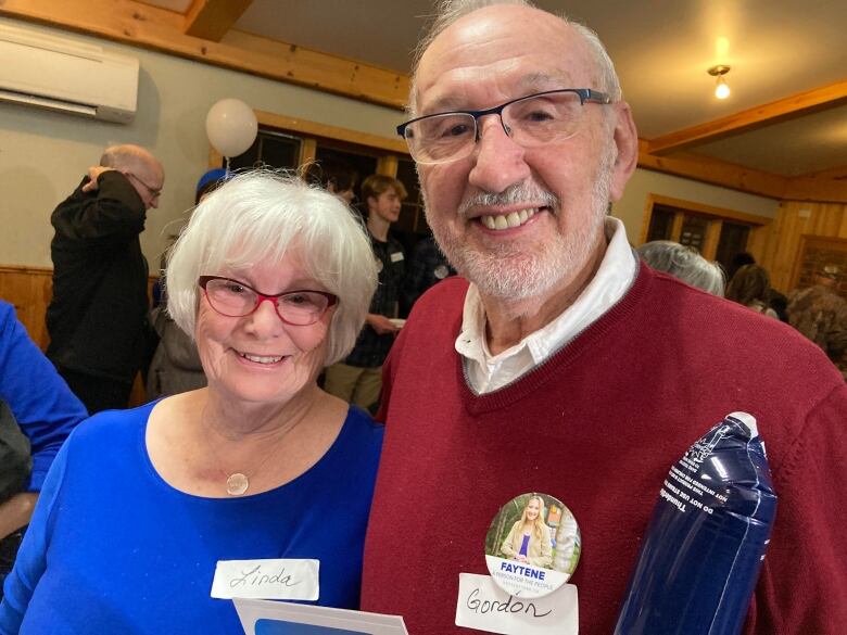 An older woman wearing blue, right, and older man wearing red, left, smiling 