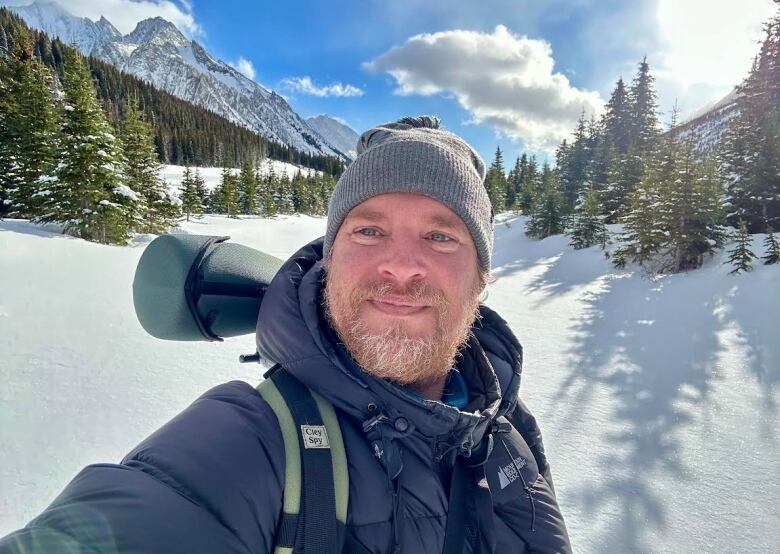 A man takes a selfie in front of snowy mountains. 