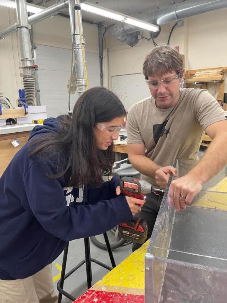 Two people wearing protective equipment work on a plastic box in a workshop.