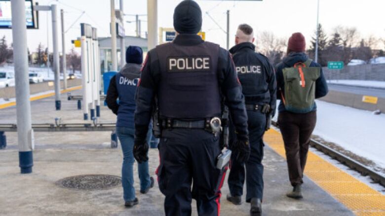 Two police officers and two outreach workers walk away from the camera on a CTrain station platform.