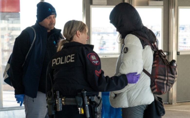 A police officer and an outreach worker talk to a person in a CTrain station shelter.