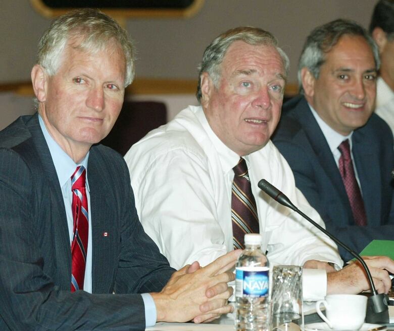 Three men sit at a table.