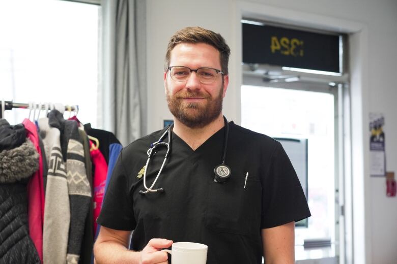 A doctor with a stethoscope and wearing black scrubs smiles.