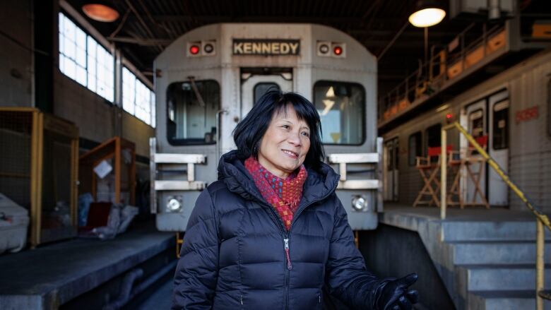 Woman in a black coat stands in front of a parked subway train.