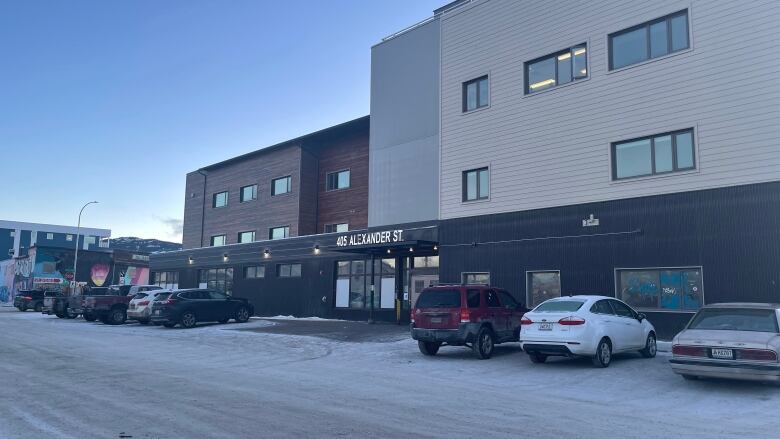 Cars are seen parked in front of a building  in winter. 