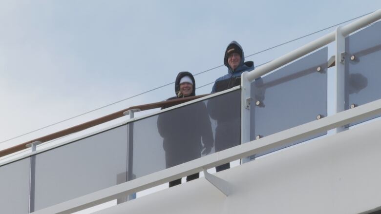 Two people look over a cruise ship as they wear winter clothing