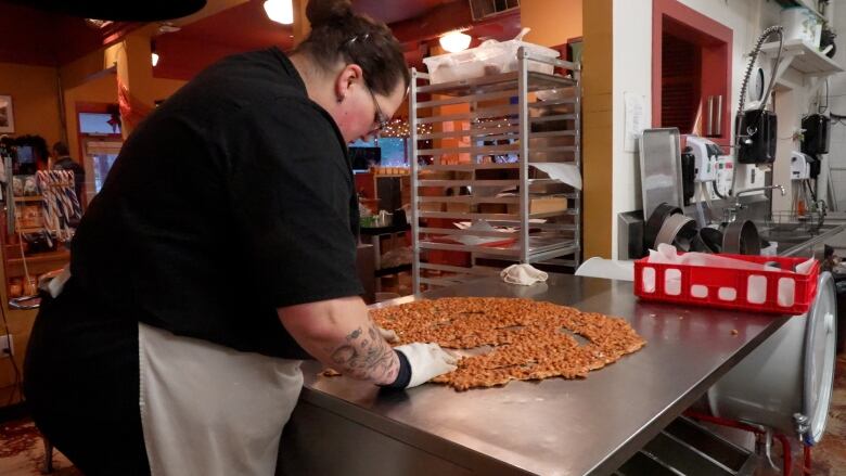 A woman stands at a metal table using her hands to work peanut brittle