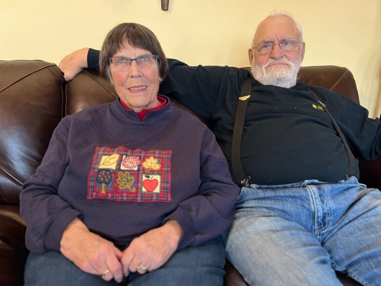 A woman and a man sit by side-by-side on a couch.