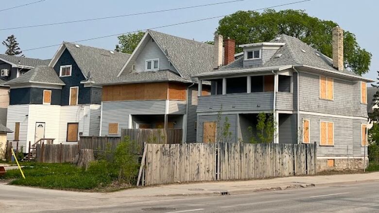 Three houses, side-by-side have their windows boarded up.