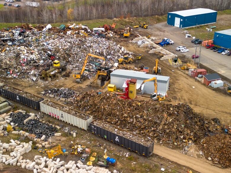 A messy site with train cars and piles of scrap material scattered around.