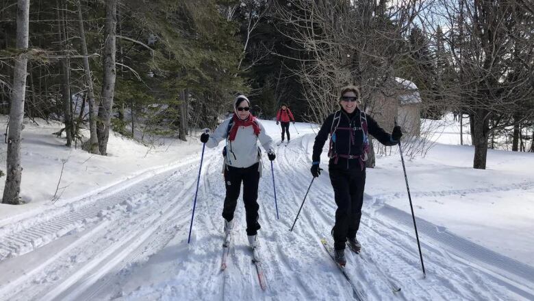 three people make their way on a snowy x-country ski path.