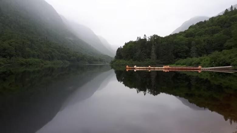 A lake and several valleyed mountain peaks are reflected in the water with birth canoes docked to the right.