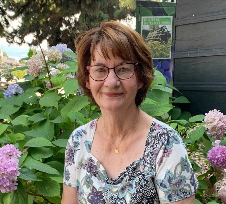 A 77-year-old woman in winged eyeglasses is outside at a garden.