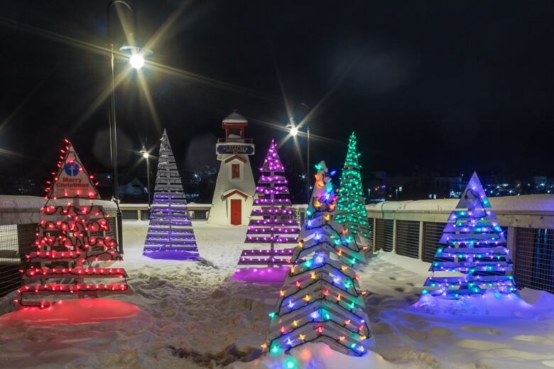 Wooden cut-out trees decorated with Christmas lights, and a lighthouse in the background. 