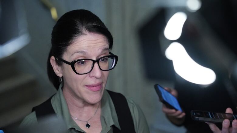 Woman wearing black-framed glasses answering questions from reporters. 