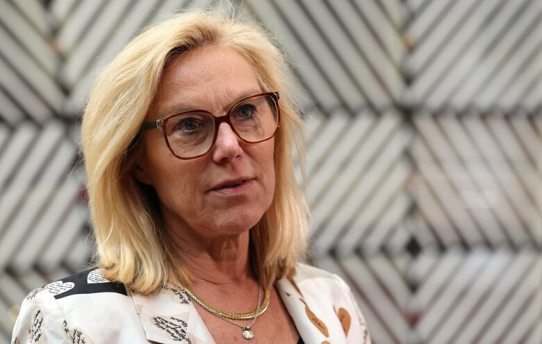 A blond woman wearing a white patterned jacket is pictured in close-up.