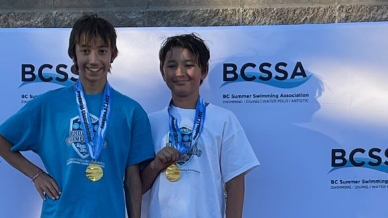 Jayden and Ashton Weiss standing on a podium showing off their winning medals from a swim meet.