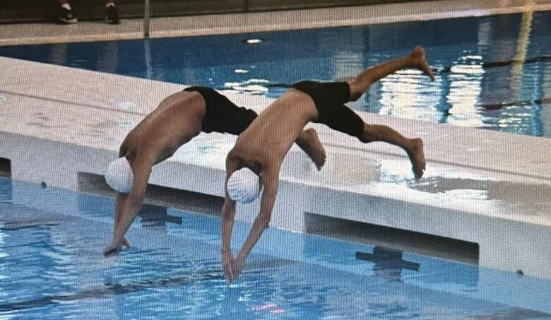 Pictured are two boys diving into the water in their white swim caps and black shorts.