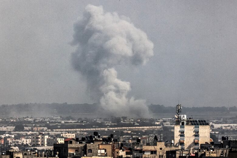 A grey-white plume of smoke towers over a cityscape.