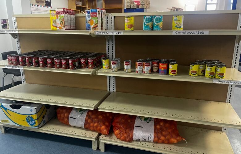 A set of shelves with some cans of food. The shelves are over half empty. 