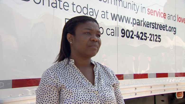 A woman looks off to the side. She is wearing a black and white polka dot shirt. She stands in front of a truck that reads 'www.parkerstreet.org'