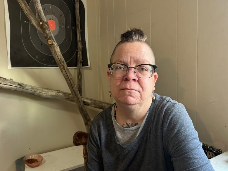 A spectacled woman sits against the wall.