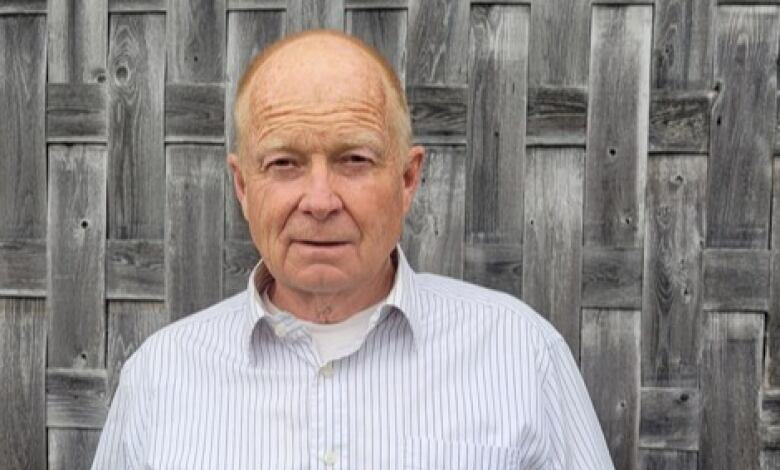 A man with a striped blue and white shirt stands in front of a wall that appears to be woven.