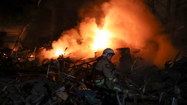 A firefighter wades through rubble as a fire rages behind him.