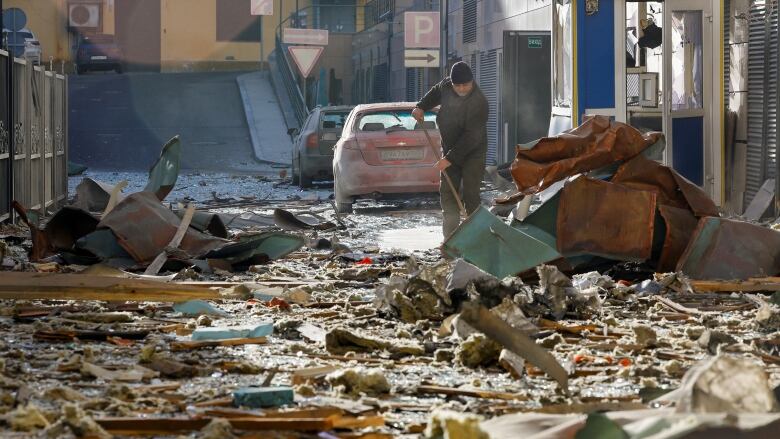 A man cleans rubble and debris in the street.