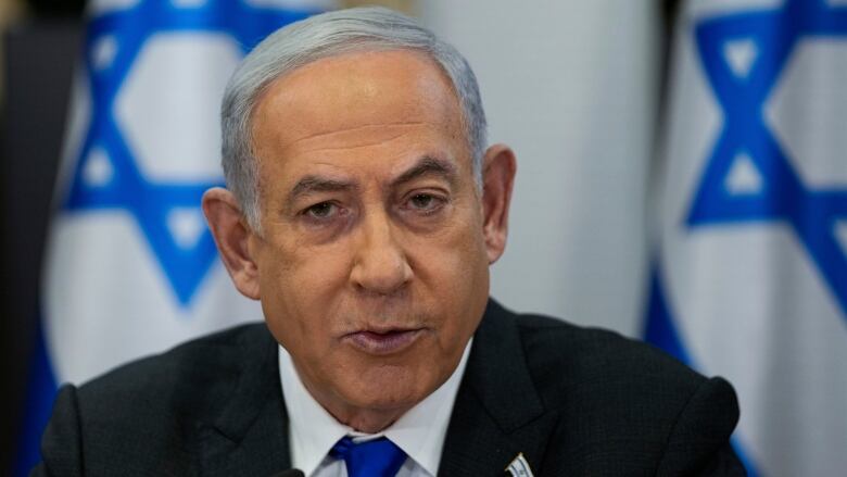 A man speaks in front of flags of Israel.