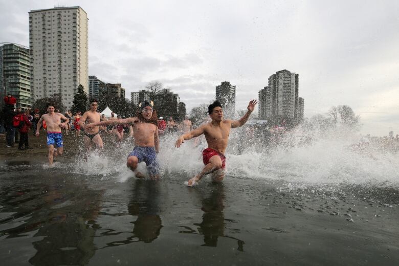 People wearing bathing suits and costumes run into beachwater, causing foam and water to splash.