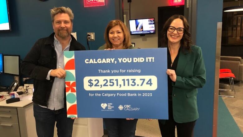 Three people hold up a board stating a total amount raised.