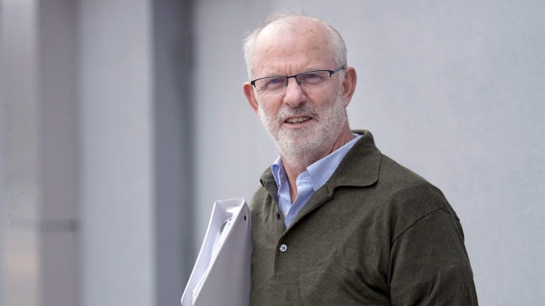 A man wearing a green sweater holds a white binder.