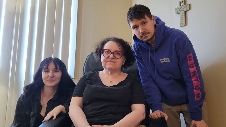 A woman sitting in a hospital-like chair with two younger people next to her.