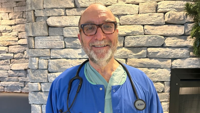 A physician with a stethoscope stands in front of a brick wall.